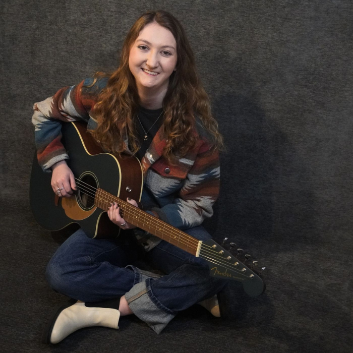 Dallas singer-songwriter Jacy Penland posing with an acoustic guitar in a promotional headshot portrait.