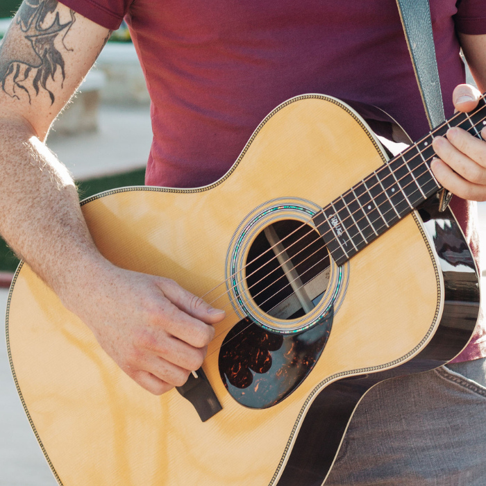 Close up of musician in a red shirt holding a guitar playing at an event.