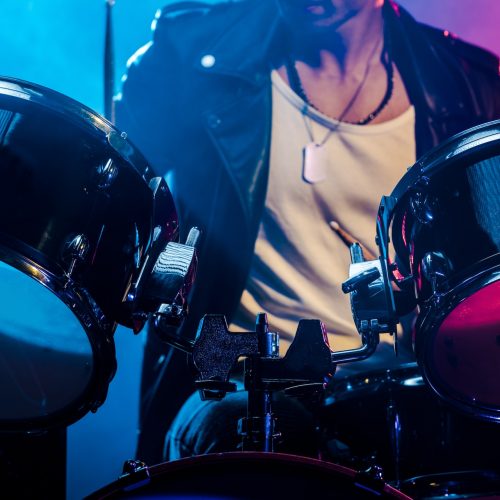 Cropped shot of male musician playing drums during rock concert on stage with smoke and dramatic