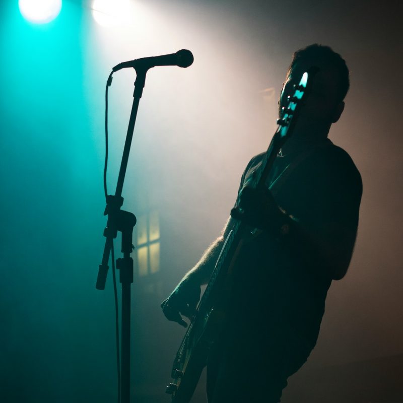 Silhouette of man on stage performing in front of a microphone with stage lights behind him