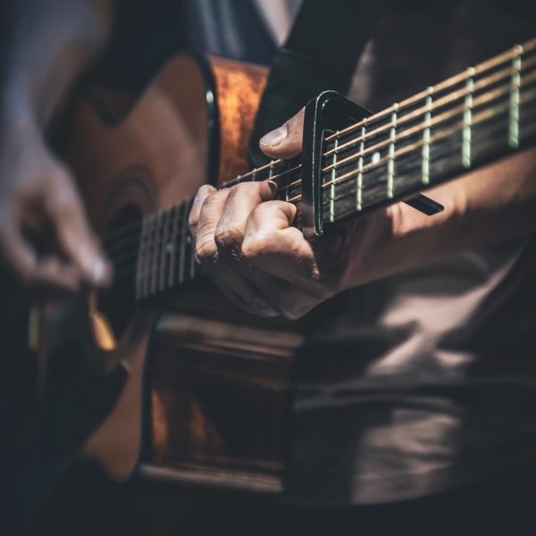 A man plays an acoustic guitar in the dark, close-up.