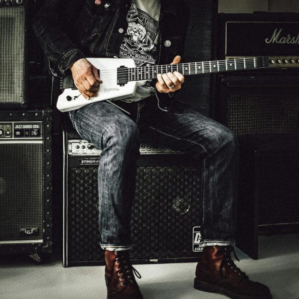 Close up of man with electric guitar sitting on top of guitar amplifiers